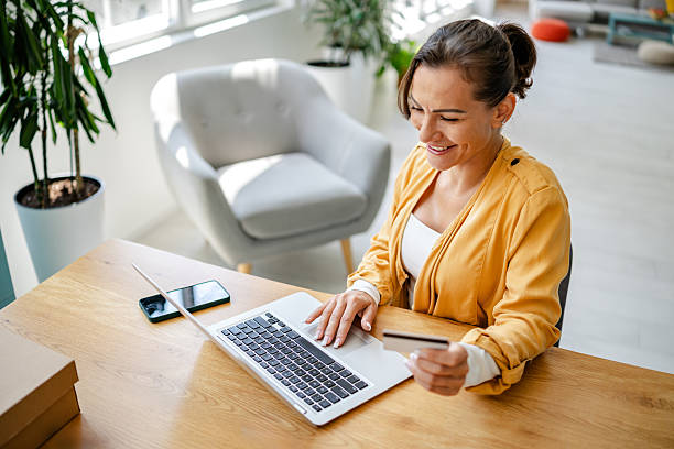 istock Woman working from home using laptop while holding a credit card in a bright and comfortable living space 2222922385