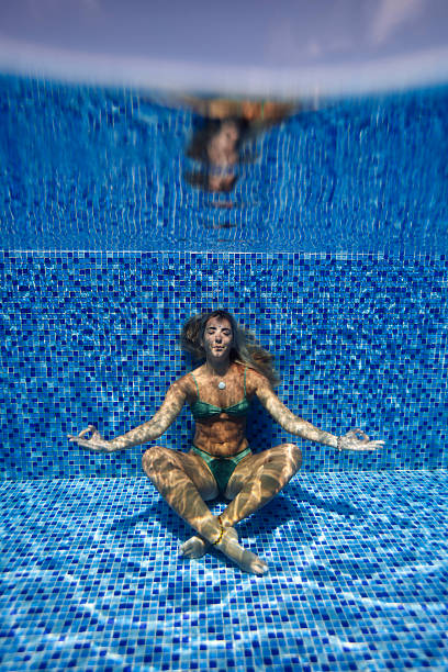 A woman in a swimsuit meditates underwater in a vibrant mosaic tile pool