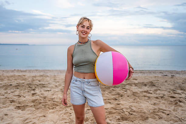 Carefree young woman enjoying summer vacation holding inflatable beach ball smiling at camera on sandy beach