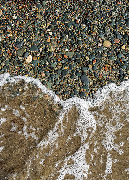 istock Wave with white foam softly lapping against pebble shoreline. Tranquil beach moment, great for calming backgrounds, spa concepts. 2222925755