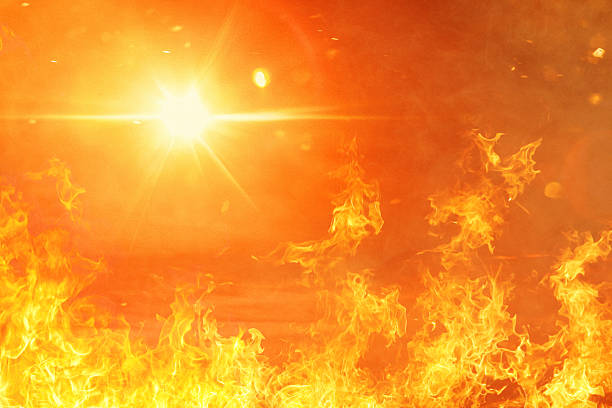 A blazing inferno of orange and yellow flames fills the frame with a brilliant sun creating lens flares in the intensely hot atmosphere. This powerful imagery symbolizes extreme summer heat waves and the growing concerns about climate change, with the overwhelming fire and solar intensity representing rising global temperatures and environmental challenges.