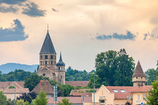 Cluny Abbey's towers rising above charming village rooftops under a cloudy sky