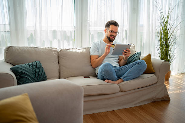istock Man sitting on sofa shopping online using digital tablet and credit card 2222938142