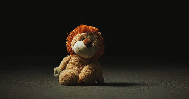 Dark, shadow and teddy bear in studio for loss, isolation and forgotten toy on ground. Night, floor and stuffed animal on black background for neglect, abandonment and unwanted with lost hope