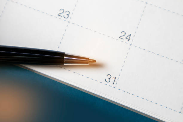 A hand holds a pen, ready to write in a blank daytimer.