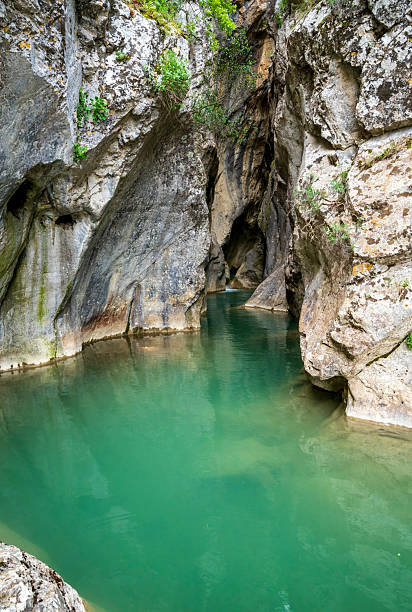 Calm turquoise water fills a narrow limestone slot, its smooth sculpted walls reflecting light inside Greece's remote Saint Luke Gorge.