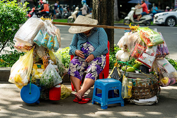 Aerial view of Vietnamese street vendor pulls a cart with food along a road with empty copy space. People wearing a traditional Asian conical straw hat, emblematic of Vietnam cultural heritage