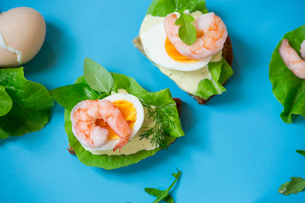 Sandwich with egg and shrimp on blue background from above.