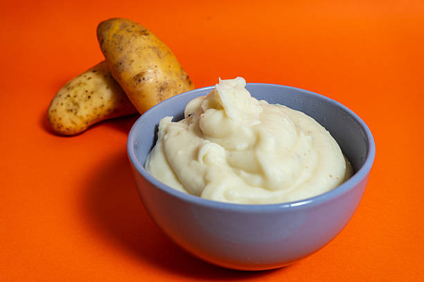 istock Mashed potatoes served in a bowl with raw potatoes aside on orange background 2222952475