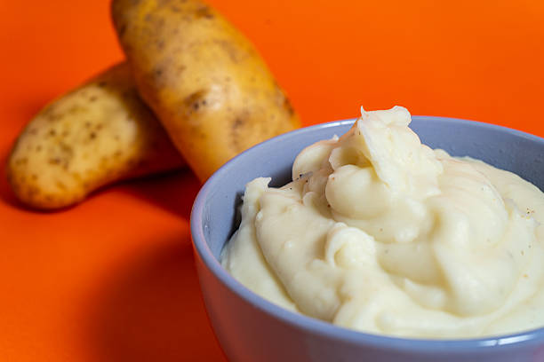 istock Mashed potatoes served in a bowl with raw potatoes on orange background 2222952507