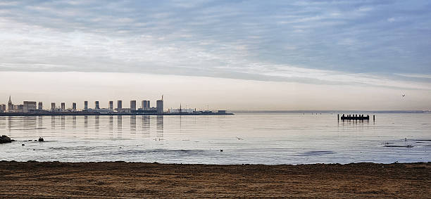 Spring landscape. Panoramic view of beautiful dawn on bay. Cumulus clouds over water in bright light. Ice, snow and rocks on coastline. Rising rays of sun are reflected in sea. High quality photo