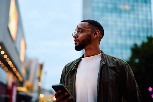 istock Young man looking away while holding mobile phone in city center 2222963857