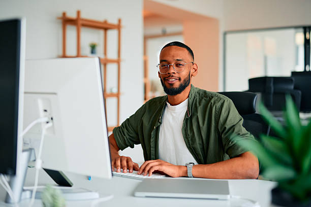 istock Young businessman typing on keyboard, looking at camera and smiling in modern office 2222964067