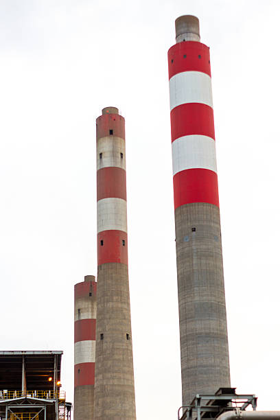 Giant industrial smokestacks with bold red and white stripes against a stark white sky. Concrete chimneys of a power plant or factory symbolizing energy, scale, and heavy industry infrastructure.