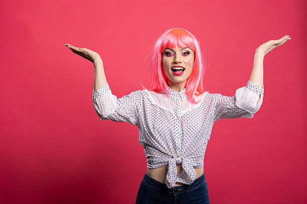 Female model with cheerful expression and open gesture presents space designed for advertisement. Joyful woman stretches arms wide, smiling brightly and standing against isolated background.