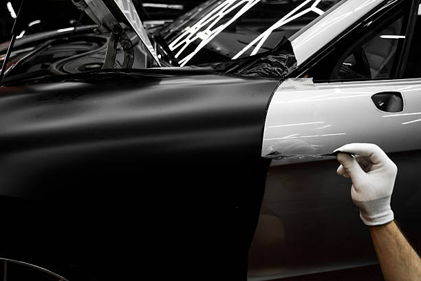 istock Full Panel Car Vinyl Wrapping. Large-scale vinyl wrap installation transforms the vehicle exterior with matte black film. Car wrap application changes vehicle appearance. 2222967868