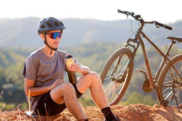 Man resting with a bottle of water next to his bike. Healthy habits, fitness, and connection with nature through cycling.