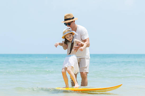 istock Girl is playing and practicing a surfboarding with her father. 2222976187