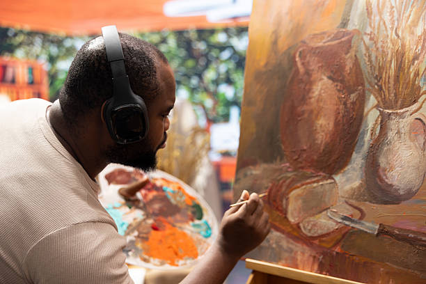 Inspired artist working on a canvas with music on headset, painting a rustic artwork using fine bristles to apply dye with precision. Creating a masterpiece with supplies in art and craft atelier.