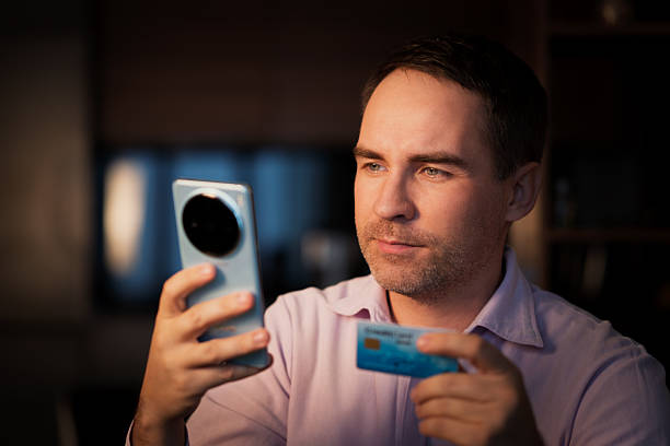 male in shirt making online payment via plastic card and smart phone. man holding mobile and credit card. Online banking. E-commerce. man enters password for his card on his smartphone. male in shirt making online payment via plastic card and smart phone. man holding mobile and credit card. Online banking. E-commerce. man enters the password for his card on his smartphone. cvc stock pictures, royalty-free photos & images