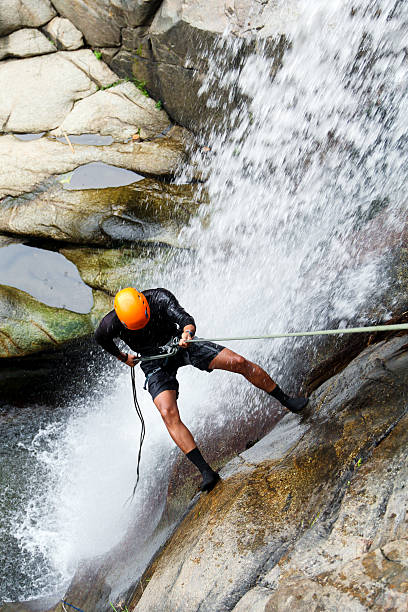 Latin hispanic adventurous canyoneer rappelling down a waterfall in a lush tropical rainforest, enjoying extreme sports and nature