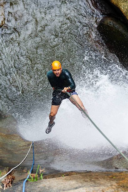 Latin american man enjoys canyoneering, rappelling down waterfall, experiencing extreme sport and thrill of nature