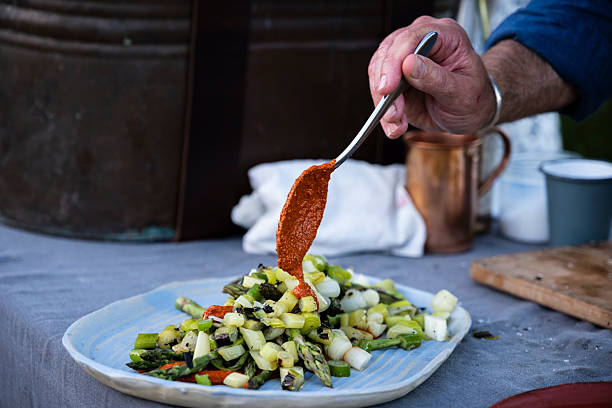 White plate with green salad, sun-dried tomatoes, hearts of palm, asparagus, with two jars of sauce on a wooden board, close-up photography