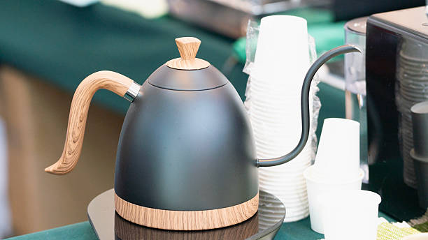 istock A sleek, modern kettle with a wooden handle sits beside disposable cups on a green tablecloth. 2222991804