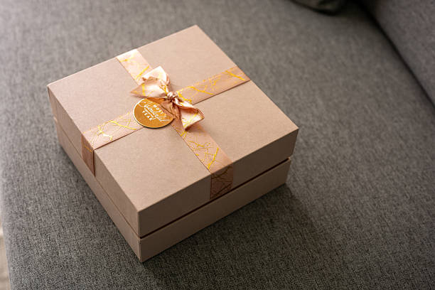 Red gift box with satin ribbon and lit heart-shaped candles on red background. Mockup of greeting card for Valentine's Day, birthday.