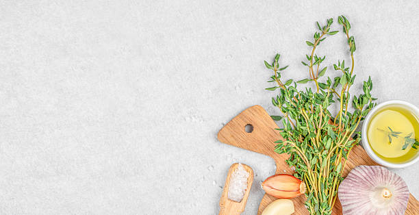 A bright culinary layout featuring fresh thyme, garlic, shallots, coarse salt, and olive oil on a light stone background, perfect for healthy cooking themes