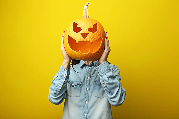 istock Female hands holding halloween pumpkin on yellow background 2222998321