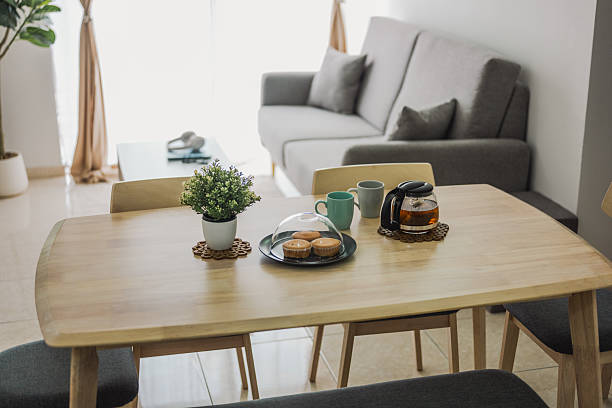 A Scandinavian-style living room showcasing a dining table set, gray sofa, coffee table, and cabinet, all set against ceramic tile flooring and a white wall backdrop.
