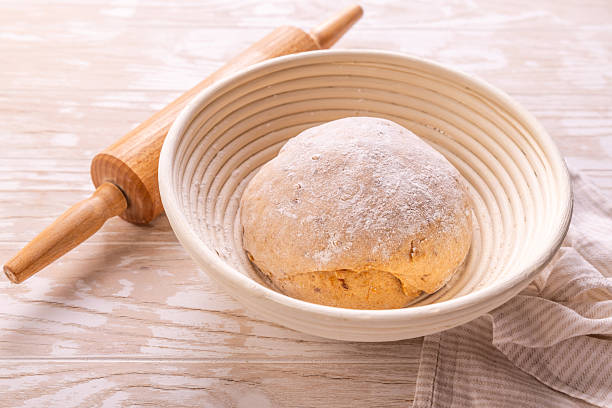 Raw yeast dough with rolling pin resting and rising in a special basket on kitchen table