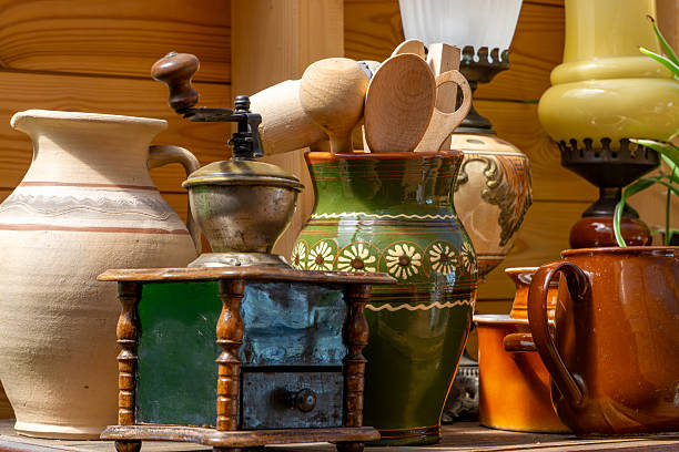 rustic kitchenware including ceramic pots, a decorative jar, wooden spoons, and an antique coffee grinder. A vintage composition evoking traditional cooking and countryside charm.