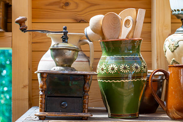 Rustic kitchen scene – vintage manual coffee grinder, wooden kitchen utensils, and traditional ceramic pottery on a wooden shelf in a cozy wooden interior. Warm natural light and countryside atmosphere.