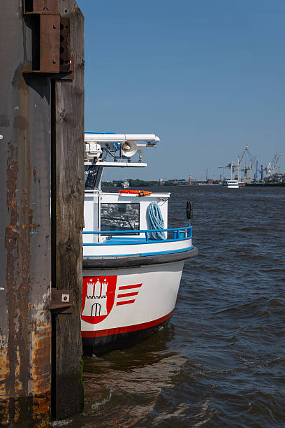 A Sightseeing Boat with a Large Hamburg City Emblem on Its Bow Waits Behind a Mooring Post to Begin the Next Harbor Tour, Capturing Tourism, Identity, and Waterfront Atmosphere