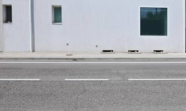 istock White plaster facade with windows of different sizes at the roadside  Concrete sidewalk and street in front. 2223008186