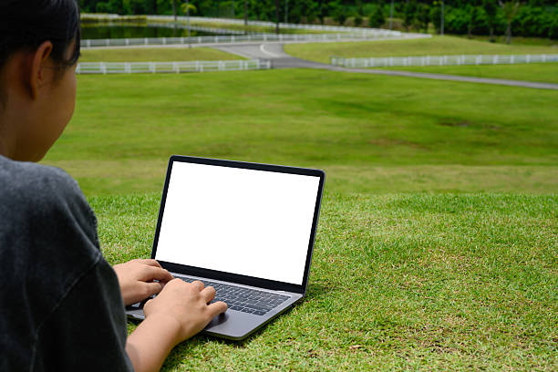 Cropped shot freelancer sitting on the grass with a blank laptop screen.