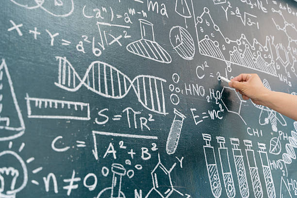 Close-up of a hand using chalk to write various scientific equations, chemical formulas, DNA structure, and lab equipment illustrations on blackboard. Ideal for education, STEM, and science learning concepts.