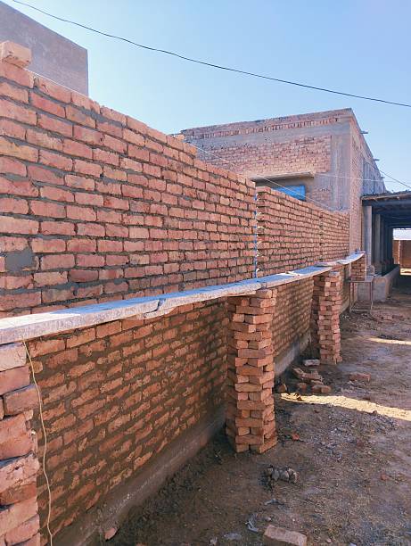 brick boundary wall under construction, ongoing construction of brick wall, building a red brick boundary wall