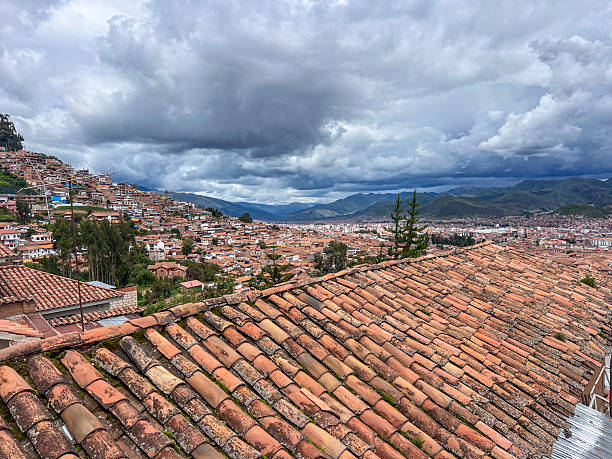 View of aged terracotta rooftops under heavy clouds in a historic city nestled in mountainous terrain. Urban landscape with traditional architecture and dramatic weather. Cityscape with cloudy sky and hills.