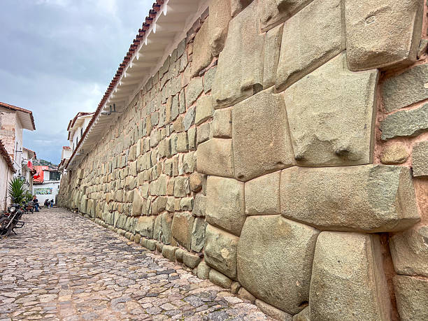 Cobblestone pathway lined by a large ancient stone wall and white buildings. Historic urban street with traditional architecture and textured stone surfaces. Old town alleyway scene.