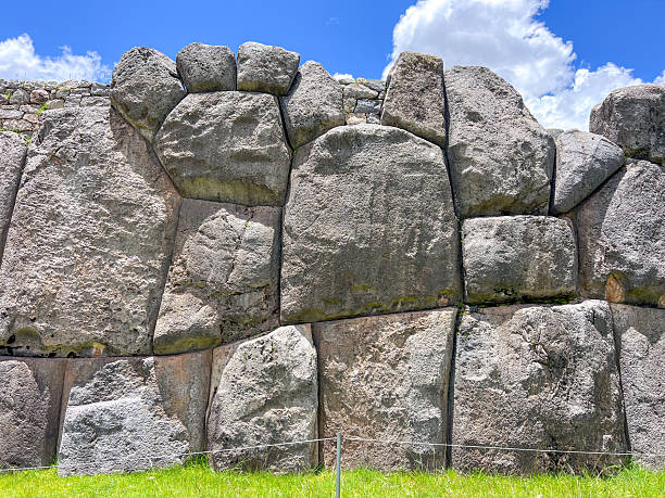 Massive interlocking stones form a historic wall at Sacsayhuaman archaeological site. Large ancient rock construction under blue sky. Famous Inca stone masonry and cultural heritage landmark.
