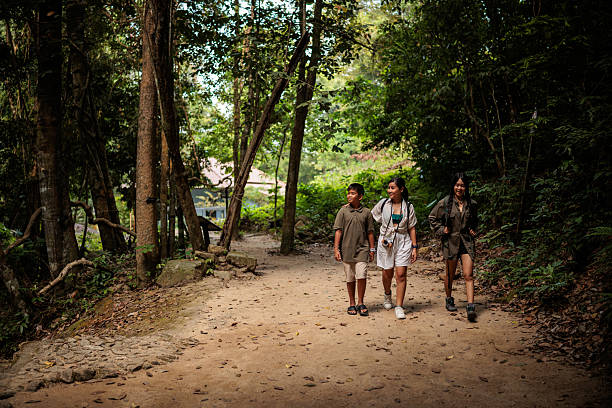 A mother, daughter, and son are walking, with backpacks on their backs,  exploring the forest of a national park in Koh Phangan, Thailand.
