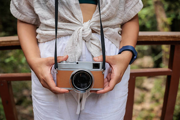 A woman holding a camera in her hands, surrounded by the lush green forest of Nacional park in Koh Phangan, Thailand.