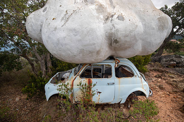 A weathered, classic Fiat 600 rests abandoned on a debris-strewn ground, its faded paint and crumbling exterior contrasting with a brick wall backdrop, evoking a sense of timeless urban decay in Bangkok's Talad Noi.