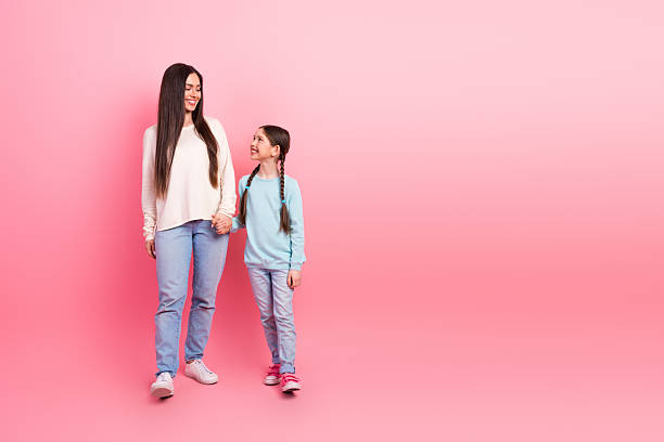 istock Mother and daughter smiling at each other while holding hands against a pastel pink background 2223037814
