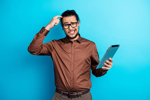 istock Young businessman with tablet exhibits confused expression against solid blue background, showcasing modern technology and formalwear. 2223039811