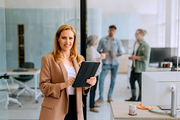 istock Well dressed mature businesswoman posing for camera while using digital tablet at modern office 2223041530
