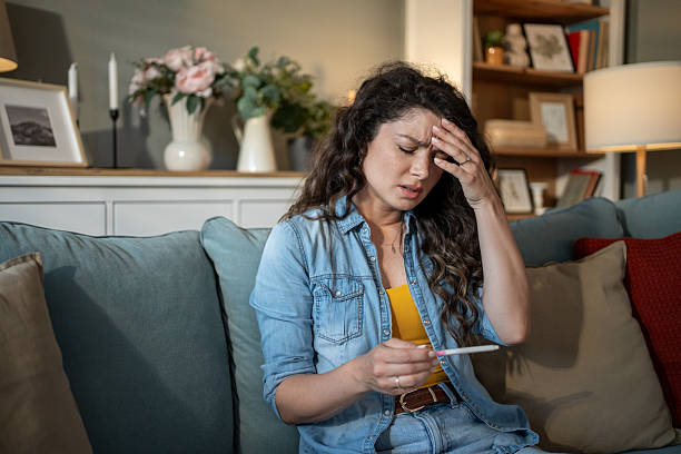 istock Young woman holding pregnancy test sitting on sofa feeling stressed 2223044044